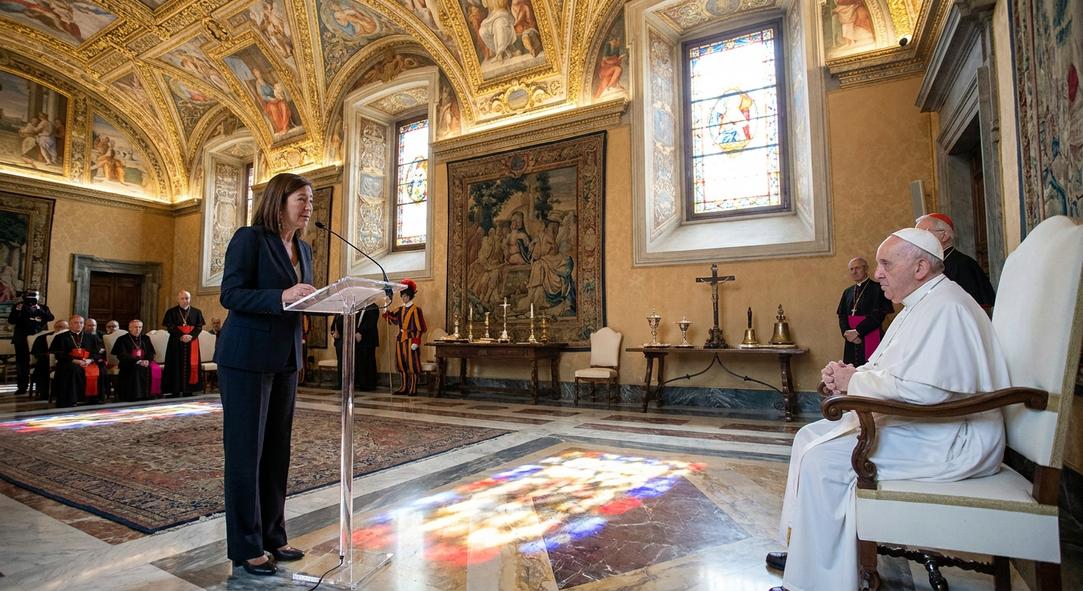 Mujer habla ante líder religioso en sala ornamentada